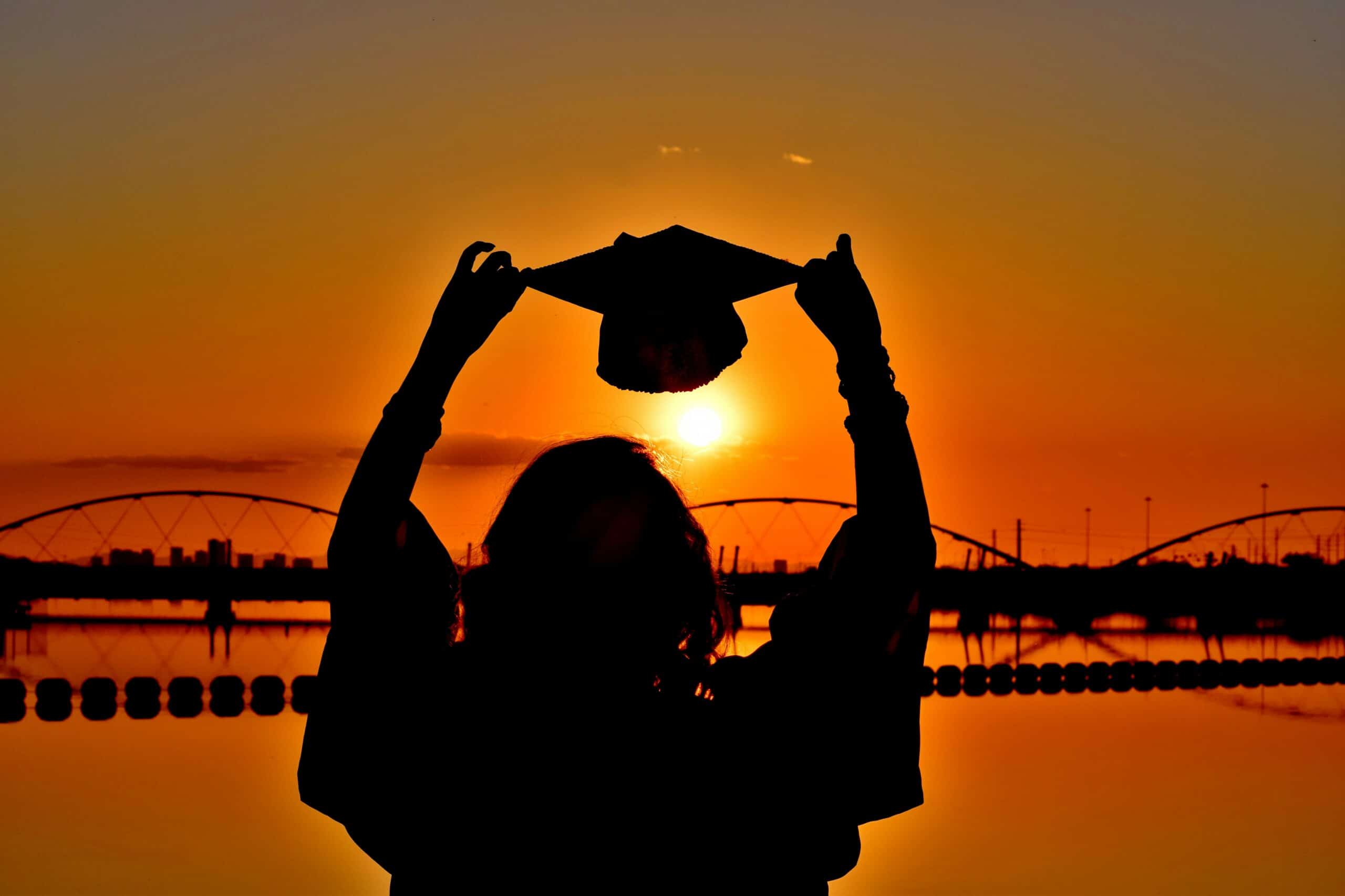 Person holding up graduation cap in sunset