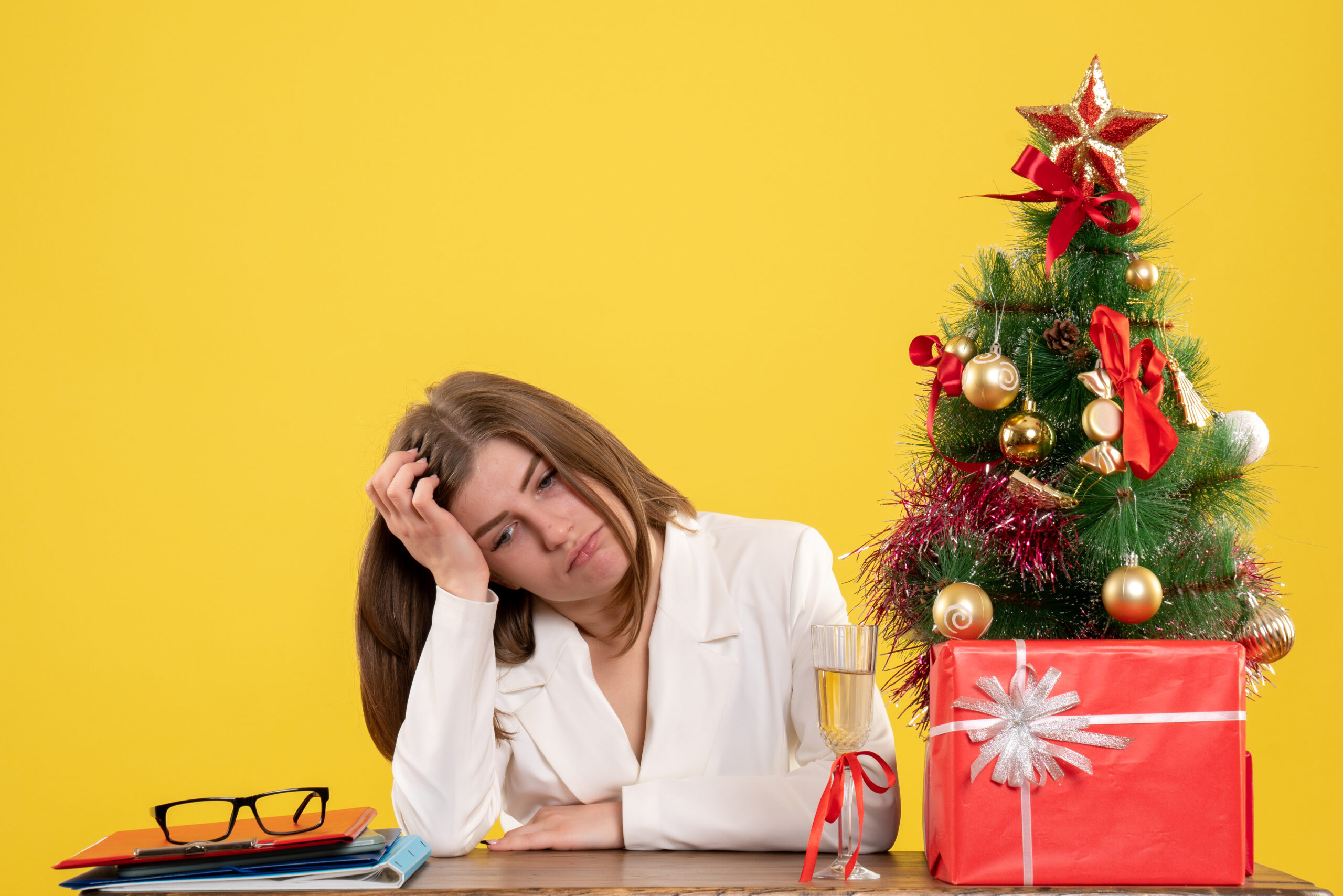 Front view female doctor sitting in front of her table on yellow background with christmas tree and gift boxes